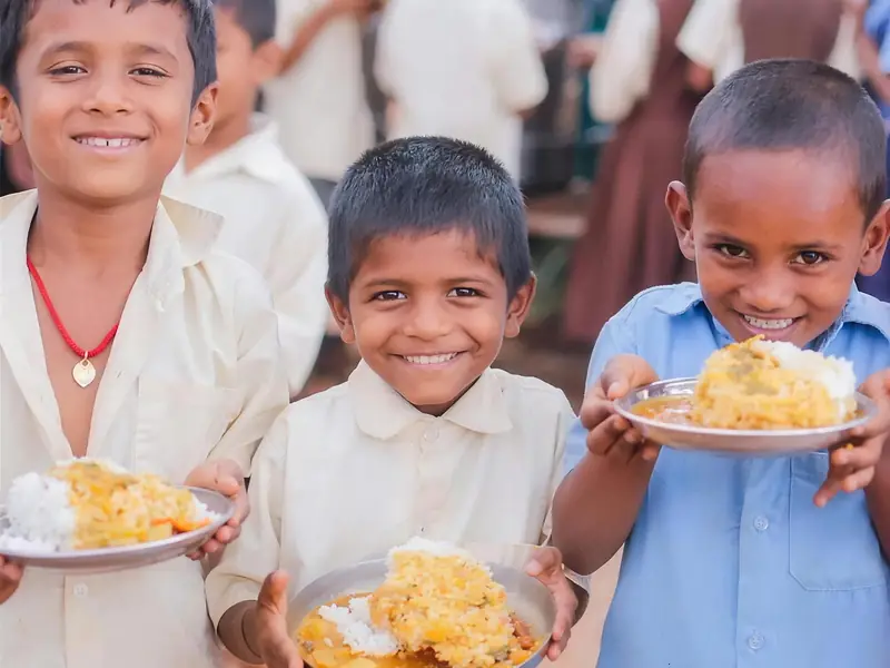 Children smiling as they hold plates of prasadam rice and sabzi